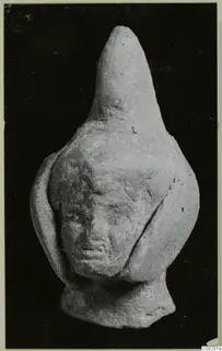Small terracotta figurine with a tall pointed top and a worn human face, photographed against a dark background.