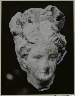 Terracotta head of a small figure with piled hair, photographed against a black background