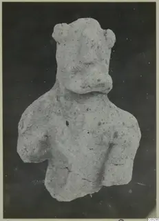 Terracotta figurine of a head and upper body with a broad nose and knob-like ears, photographed against a dark background