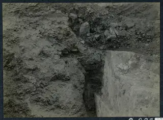 Excavated trench at Soli showing a layered soil face, loose stones in the spoil, and a squared stone block on the right.
