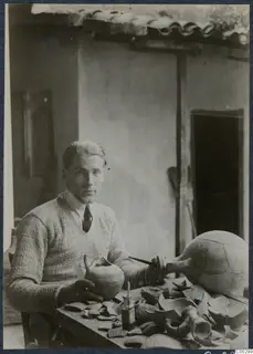 Alfred Westholm seated at a table repairing broken pottery vessels in front of a whitewashed building.