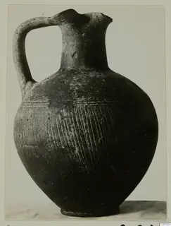 Pottery jug with a strap handle, a pinched mouth and closely spaced incised lines on its body