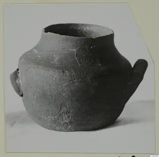 Black-slipped pottery jug with a wide mouth, a small lug handle on the left and a tall loop handle on the right.