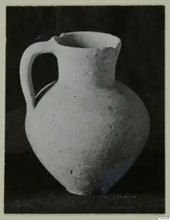 Pale pottery jug with a single loop handle, photographed against a dark background