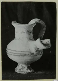 Pale clay vessel with a side spout, a loop handle and dark painted bands, photographed against a dark backdrop