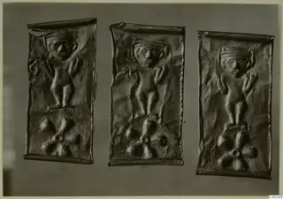 Three embossed thin metal plaques, each with a relief figure with raised arms above a rosette motif.