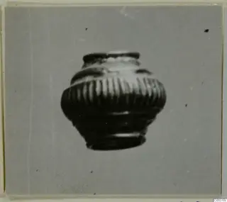 Small ribbed jar with a narrow mouth and moulded bands around the shoulder, photographed on a grey background