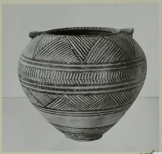 Painted pottery vessel with two small handles, banded with hatched triangles and chevrons, shown from the side.
