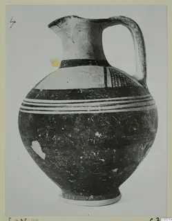 Pottery White Painted I jug with a high handle, dark bands and white painted zones on a rounded body.