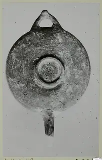 Plain clay oil lamp seen from above, with a loop handle at the top and a nozzle at the bottom.