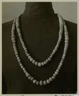 Two strands of pale, speckled beads draped over a dark stand, from the Lapithos Vrysi tou Barba tombs