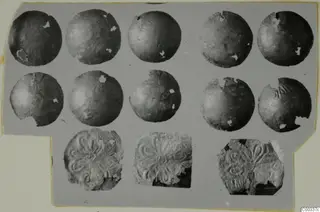Ten thin round gold discs and three embossed gold pieces with a radiating petal-like pattern, shown on a grey card