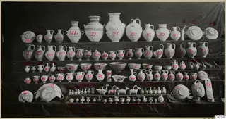 Rows of pottery vessels from Lapithos Tomb 403 displayed on tiered shelves, with red numbers painted on many pieces