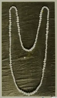 Necklace of pale round beads of varying sizes laid out on dark crumpled cloth