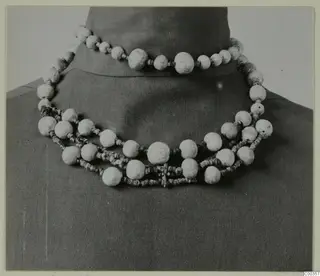 Necklace of large pale beads and small dark beads, draped over a dark bust, from the Lapithos Vrysi tou Barba tombs