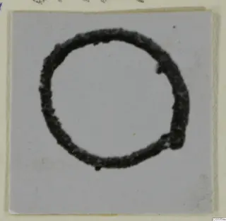 Dark ring-shaped bronze object on a light grey card.