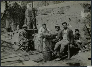 Four men and a boy take a break at a wooden table outside a mud-brick wall.