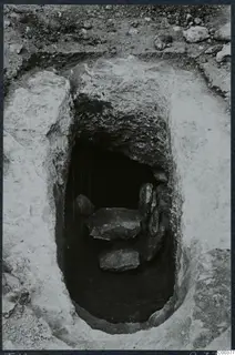 Rock-cut tomb 10 at Milia seen from above during excavation, with flat stone slabs inside the chamber opening