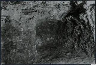 Interior of Tomb 13 at Milia during excavation, with rough rock walls and an uneven floor.