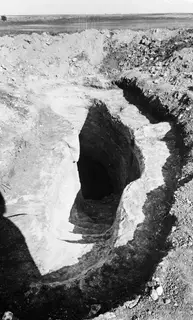 Tomb 12 at Milia: a sloping dromos cut into pale soil, leading down to the dark entrance of the tomb chamber.