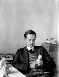 Einar Gjerstad seated at a table, holding and looking down at a small pale figurine in his hands.