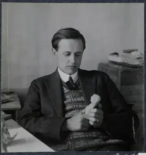 Einar Gjerstad seated at a desk, holding and looking down at a small pale object in his hands.