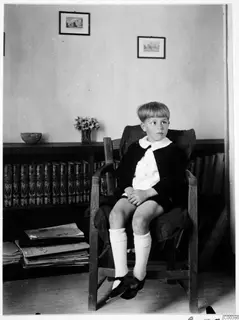 Martin Gjerstad seated in a wooden armchair beside a bookcase of leather-bound books, on Gladstone Rd