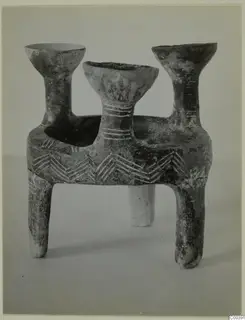Red Polished pottery tripod vessel with three flaring bowl-shaped mouths on tall necks, set on three short legs.