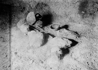 Tomb 317 interior at Lapithos, with broken pottery, a small bowl and large stones on the earthen floor
