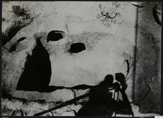 Tomb 307 at Vrysi tou Barba, Lapithos, during excavation, showing two openings in a pale rock surface with grass at the edge.