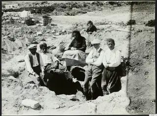 Excavation at Lapithos with baskets and a group of adults and a child posed in and around a pit