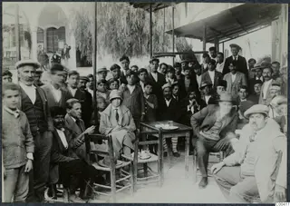 Group of men and one woman gathered on a covered terrace at a kafeneion in Kalavasos, seated around a small wooden table.