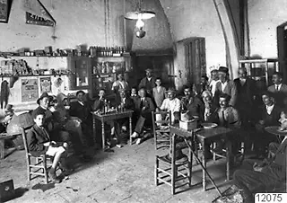 Group of men in a café interior at Lapithos, seated and standing around small wooden tables
