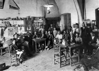 Café interior at Lapithos with a group of men seated at small tables and standing around the walls