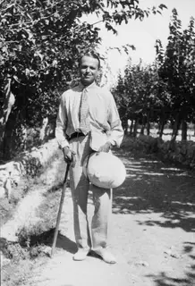 Erik Sjöqvist standing on a tree-lined dirt road at Lapithos, holding a walking stick and a straw hat