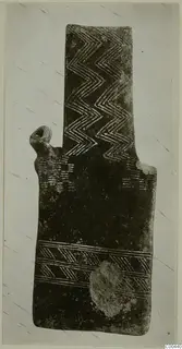 Plank-shaped figurine, back view, with incised zigzag and chevron patterns on a dark surface.