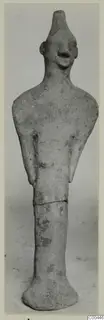 Standing terracotta figurine with a tall cylindrical head, pinched nose and arms held close to the body, seen from the front.