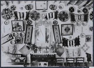Interior of a house at Milia, a wall covered in embroidered textiles, plates, a mirror and a hanging lamp