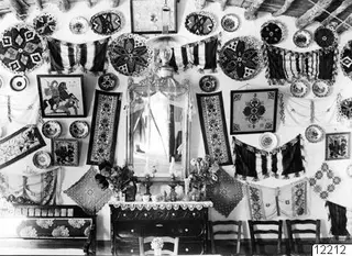 House interior at Milia with a wall covered in plates, embroidered textiles, framed pictures and a central mirror