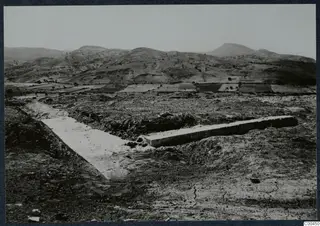 Excavated terrace at Soli with long stone wall foundations, with hills and cultivated fields beyond