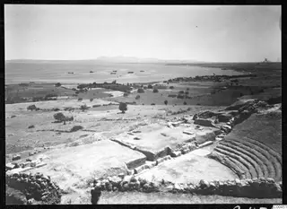 The theatre at Soli, with curved tiers of stone seating and walls, overlooking a bay with anchored boats.
