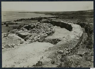 Ruined curved walls of the theatre at Soli, with the sea and a village on the shore beyond