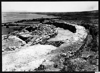 Ruined stone walls and rubble on a hillside at Soli, with the sea and shoreline beyond.