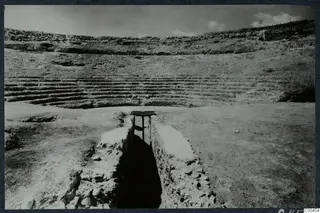 Excavated stone seating steps of the theatre at Soli, with a narrow walled passage cut through the foreground