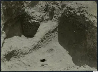 Excavation trench at Soli with cut soil faces, loose stones and a digging tool handle visible.