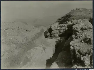 Excavation trench at Vouni Palace cutting between rock and stone masonry, with a hazy view of plains beyond.