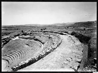 Curved rows of stone seating and a retaining wall at the theatre at Soli, with an open plain and hills beyond.