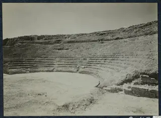 Excavated theatre at Soli with curved rows of stone seating stepping up a hillside around a flat central area.