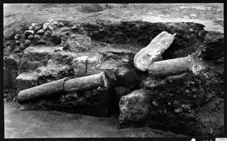 Excavated trench at Soli theatre with two cylindrical stone column drums and a carved stone fragment among walls