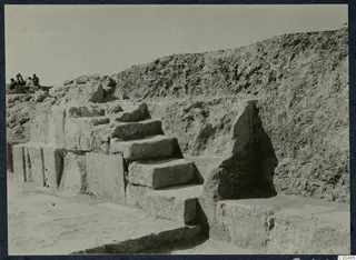 Stone steps of cut blocks rising against an excavated earth bank at the theatre at Soli, with people at top left.